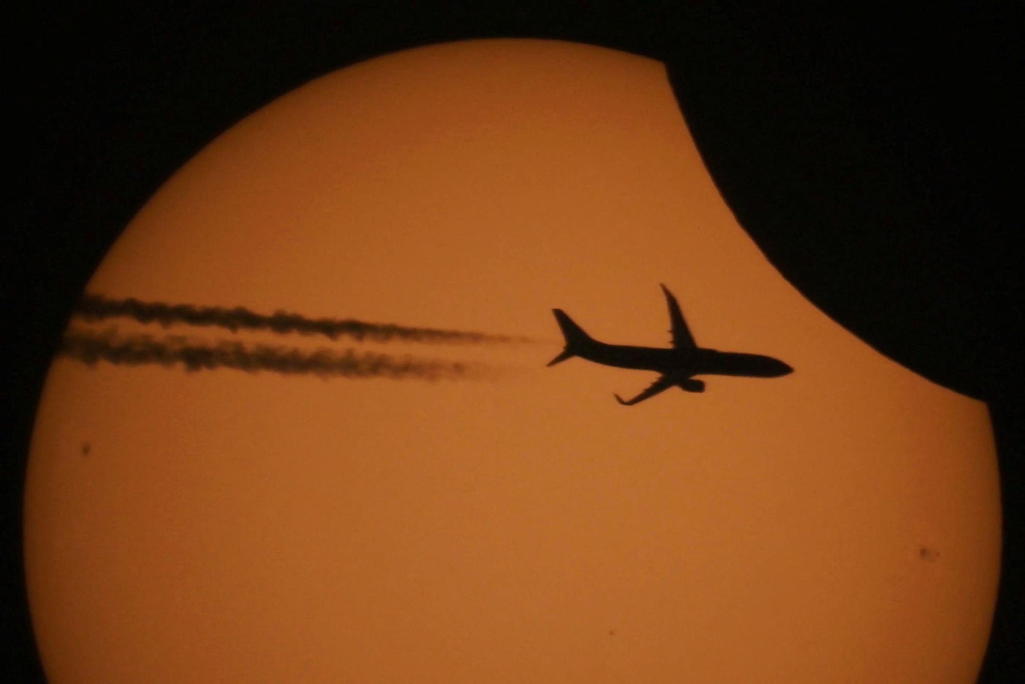 A plane is silhouetted against the sun during a partial solar eclipse in Kojori