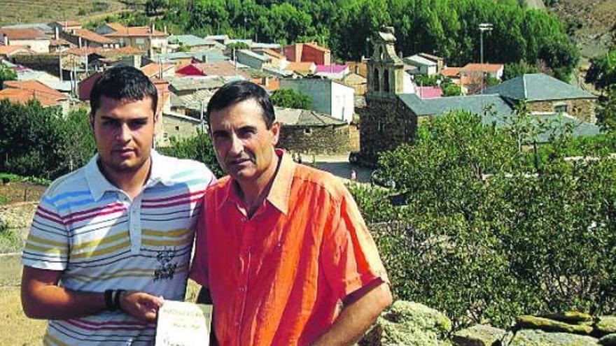 Alejandro y José Luis Argüello posan con su libro. Al fondo, el pueblo de Manzanal del Barco.