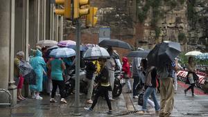 Diversos ciutadans es protegeixen de la pluja, aquest diumenge a Barcelona.