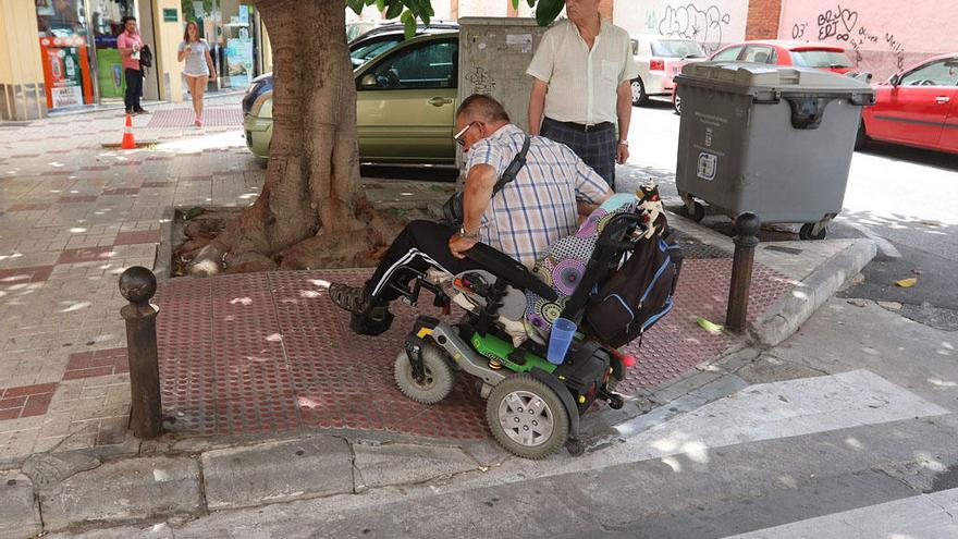 Un vecino con silla de ruedas eléctrica sube el rebaje del paso de cebra, bloqueado en parte por el ficus.