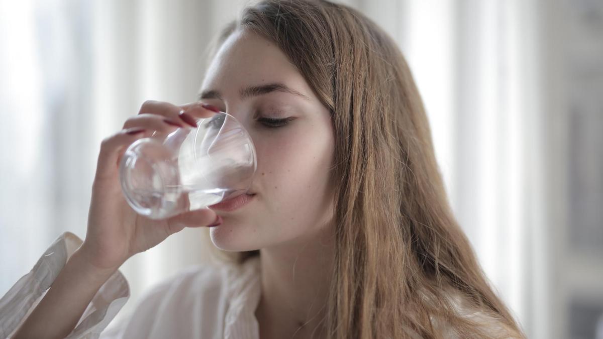 Una joven bebe un vaso de agua.
