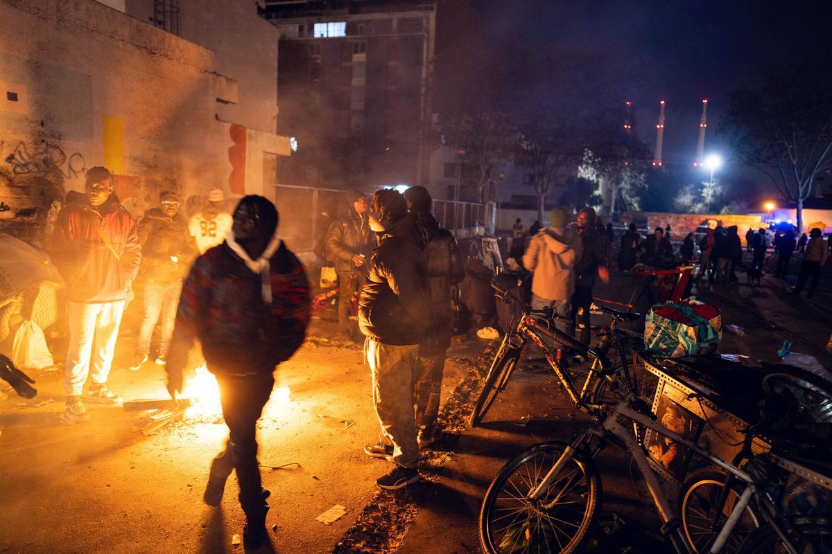Badalona, 17/12/2025. Sociedad. Personas desalojadas del antiguo instituto B9 se concentran en la plaza frente al edificio, preparando enseres y refugios improvisados para pasar su primera noche durmiendo en la calle tras el desalojo. Foto: Zowy Voeten / El Periódico