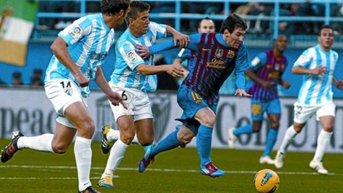 Mathijsen (14) y Camacho (6) intentan frenar a Messi, que inicia la carrera en la que acabaría marcando su tercer gol, ayer en La Rosaleda.