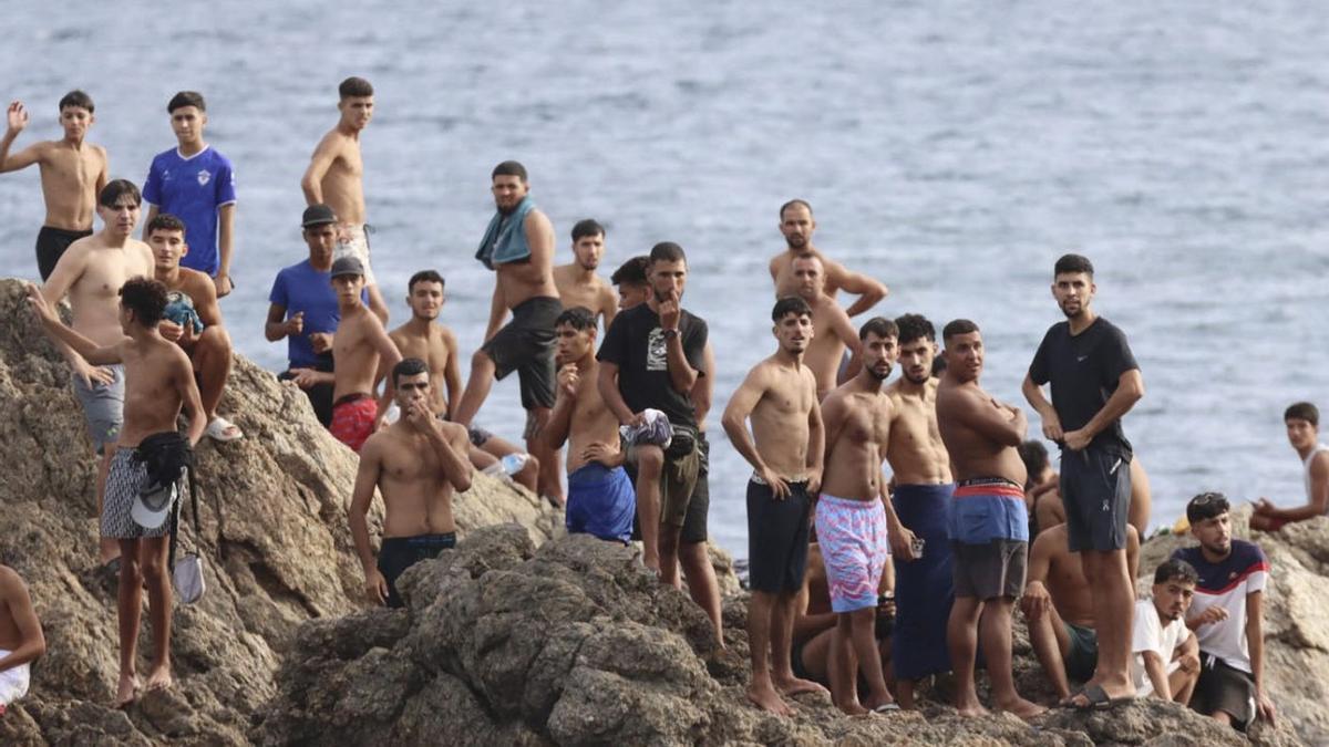 Migrants observen des de les roques de la platja Juan XXXIII de Ceuta, ahir. | REDUAN / EFE