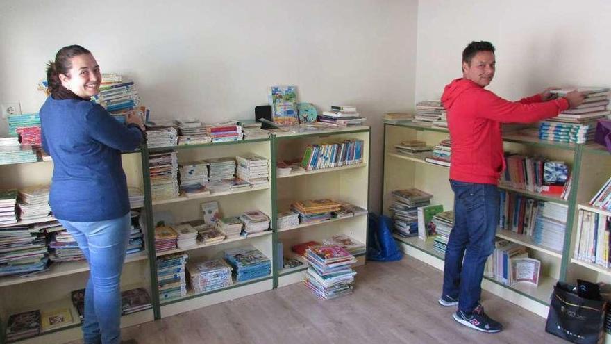 Dos profesores colocan los libros en la biblioteca, trasladada a la antigua casa del conserje.