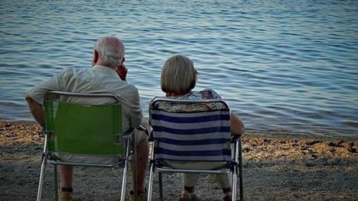 Una pareja de jubilados descansa en una playa.