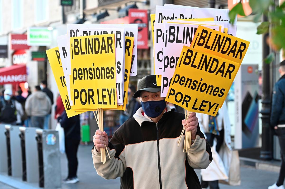 Un hombre sostiene varias pancartas, durante la manifestación a favor de blindar las pensiones en Madrid.
