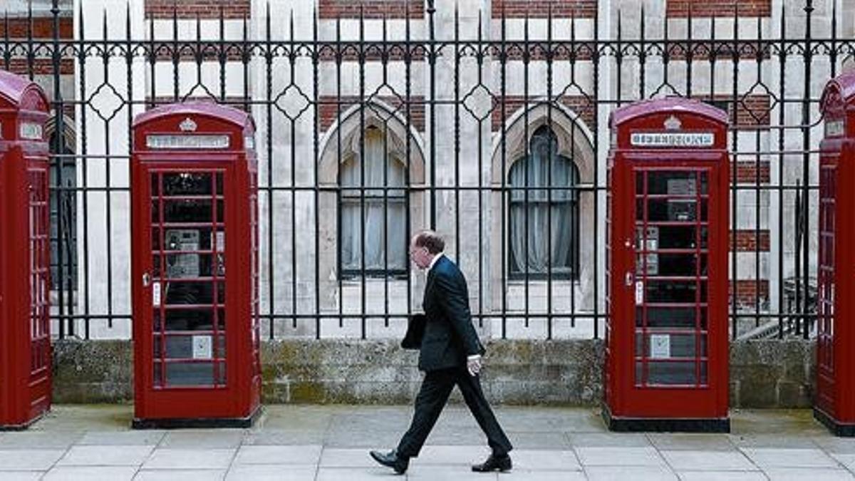 Un hombre trajeado camina por una calle londinense con distintos modelos de las clásicas cabinas de teléfono británicas.