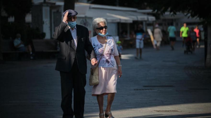 Dos personas mayores caminan con mascarilla por una calle de Los Cristianos, en el municipio tinerfeño de Arona.