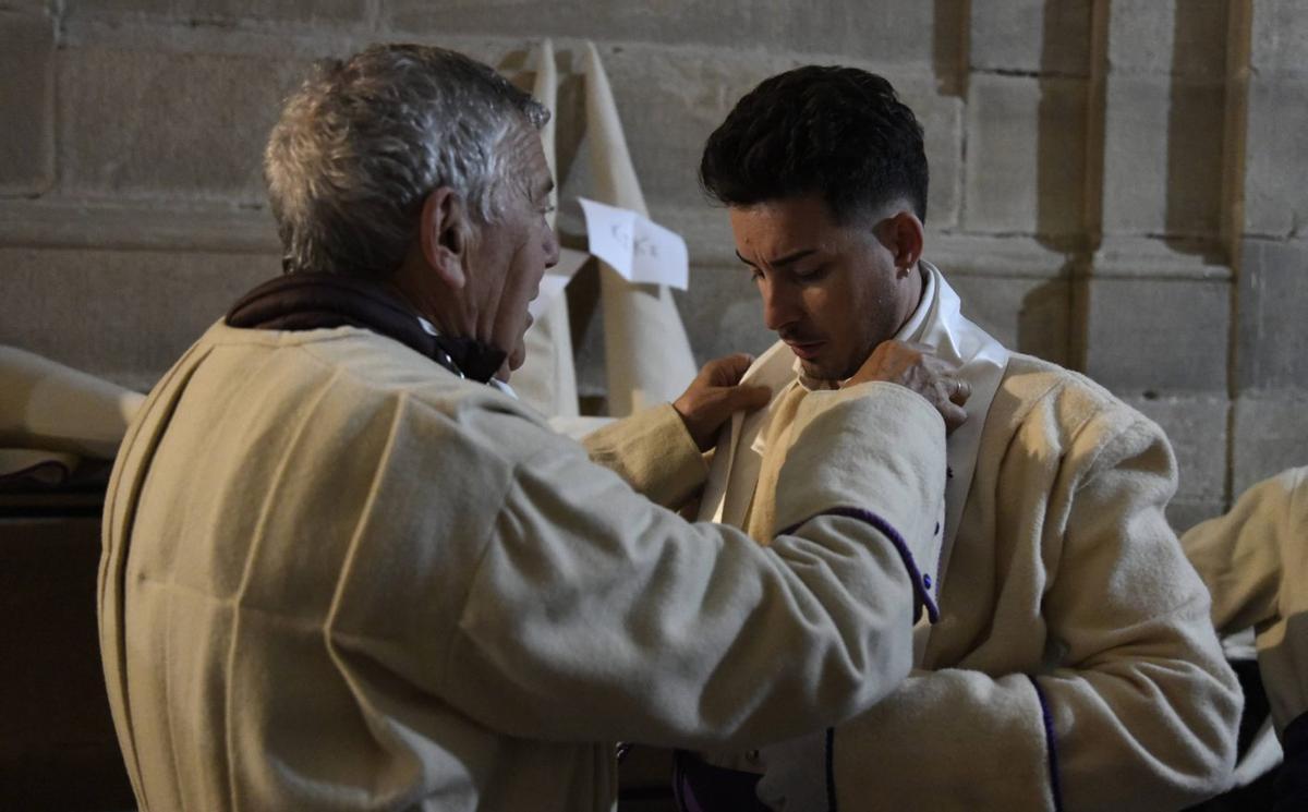 un hermano del Yacente ayuda a otro más joven a ponerse el pañuelo en la procesión del pasado año.