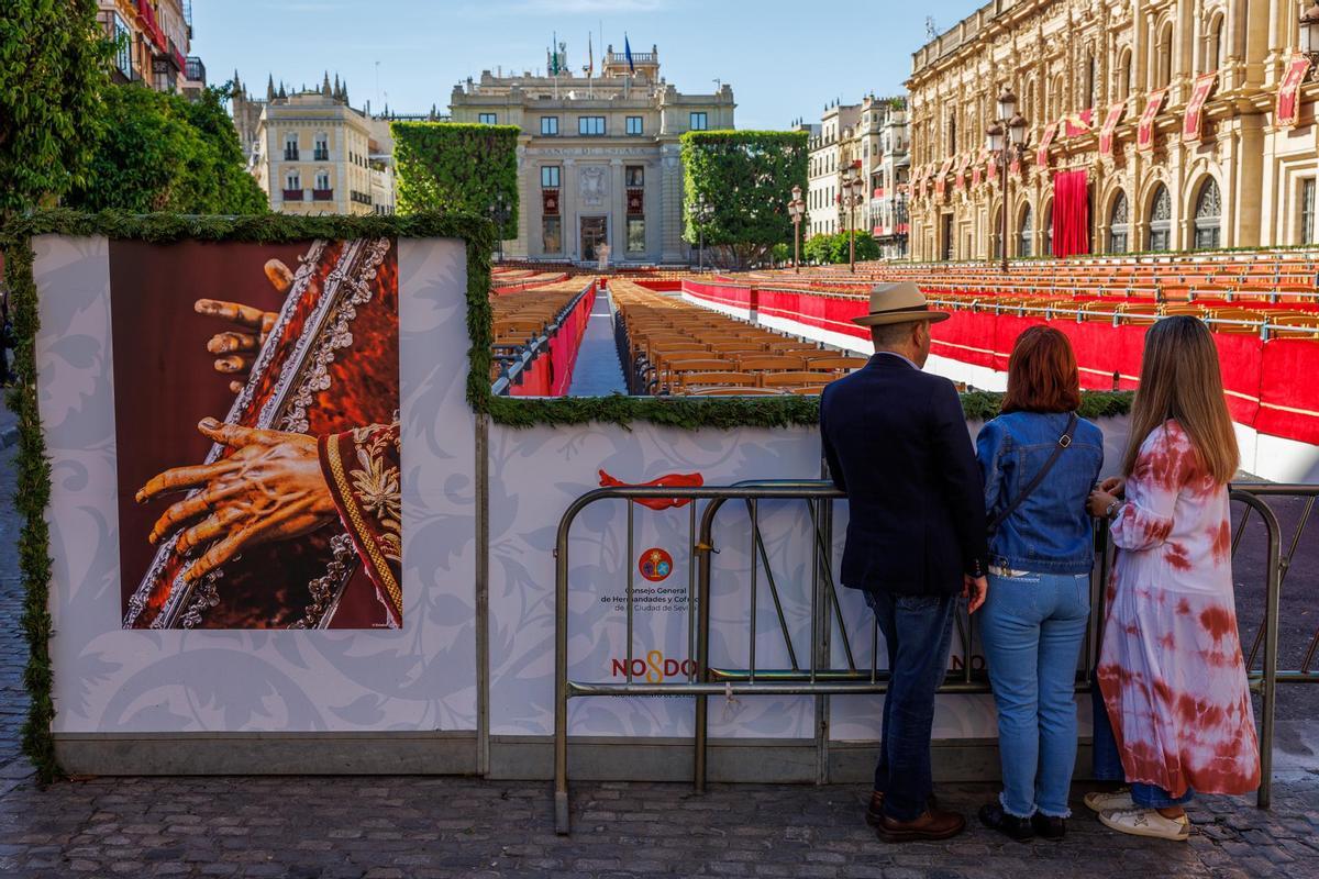 Unos turistas observan los palcos vacíos de la carrera oficial de las procesiones de la Semana Santa de Sevilla, recorrido obligado por el que a partir de mañana discurrirán los pasos y los nazarenos de las nueve Hermandades que hacen estación de penitencia en Domingo de Ramos.