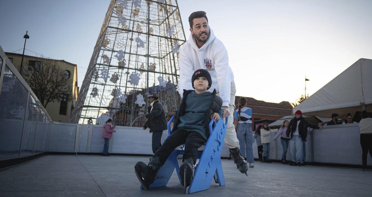 Un adulto y un niño patinan sobre la pista de hielo artificial instalada en la  Plaza de la Navidad.