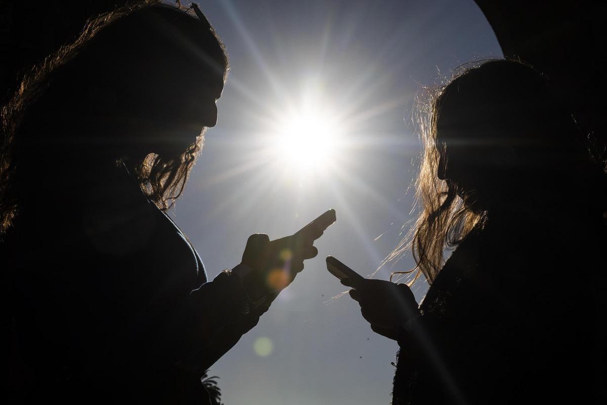 Dos adolescentes, con sus móviles.