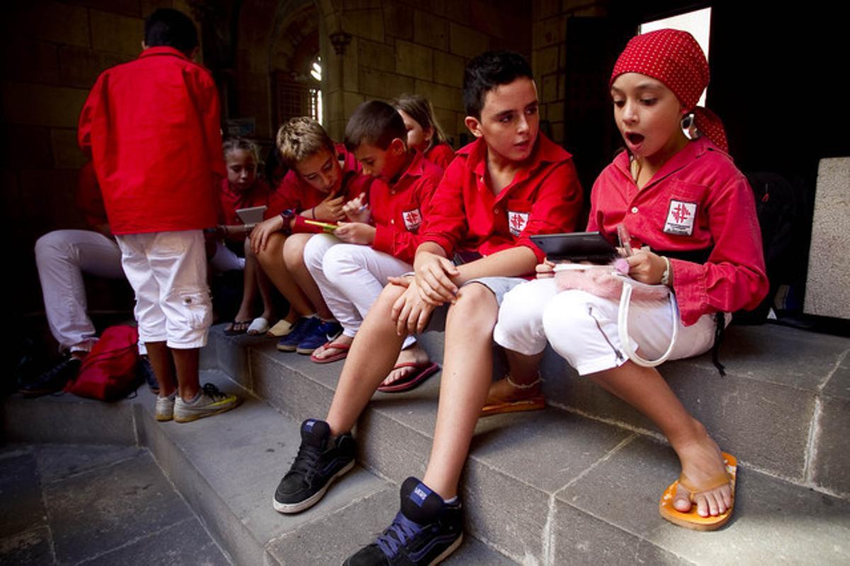 Els més petits de la colla dels Castellers de Barcelona, es diverteixen amb jocs electrònics, aliens a la multitud reunida a la plaça de Sant Jaume.