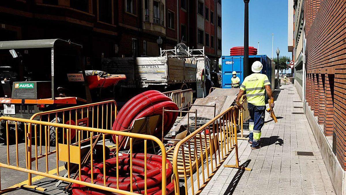 Obreros trabajando mientras pasan camiones y excavadoras por la calle Caridad.