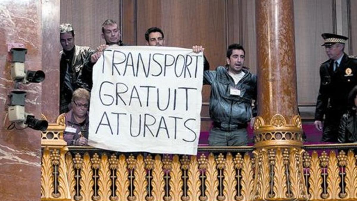 Unos vecinos exhiben una pancarta pidiendo transporte gratuito para los parados en el salón de plenos del Ayuntamiento de Barcelona, ayer.