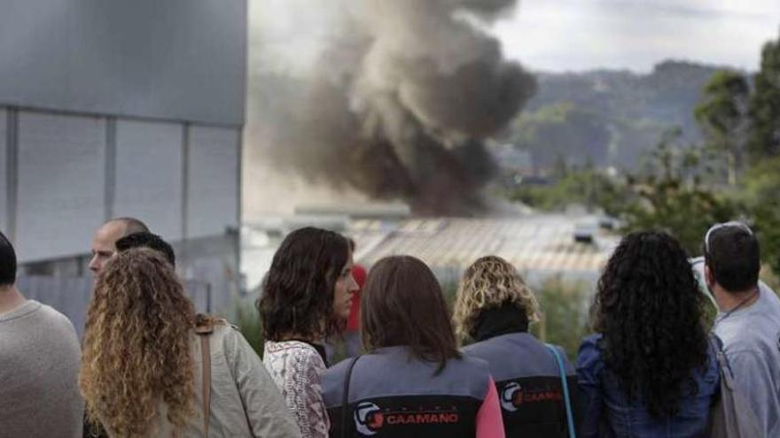 Trabajadores evacuados miran la nube de humo mientras efectivos de extinción apagan el incendio.