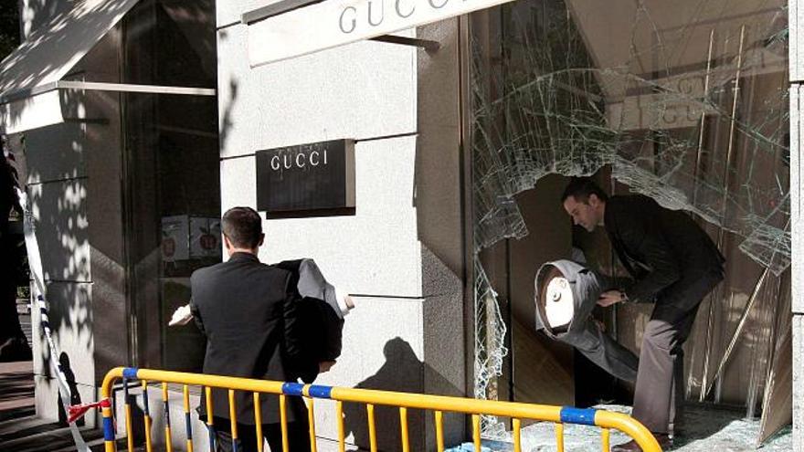 Dos empleados retiran la ropa del escaparate de la tienda que sufrió un alunizaje ayer en Madrid.