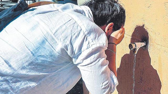 Una mujer se refresca en una fuente pública.