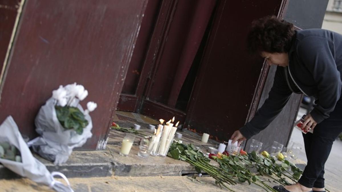 Una mujer deja velas y flores en la puerta del bar Carillon, situado en el décimo distrito de París.