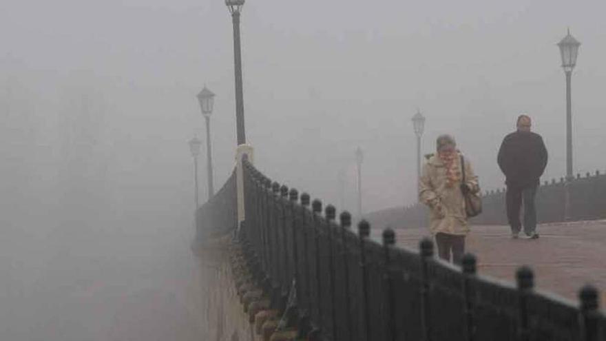 Dos viandantes caminan por el Puente de Piedra en medio de una intensa niebla.