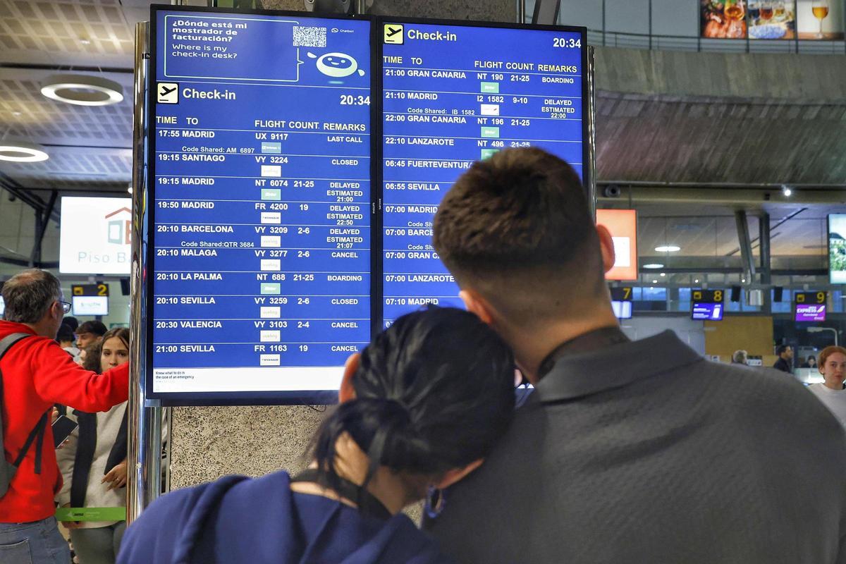 Dos jóvenes frente a un panel informativo del aeropuerto.
