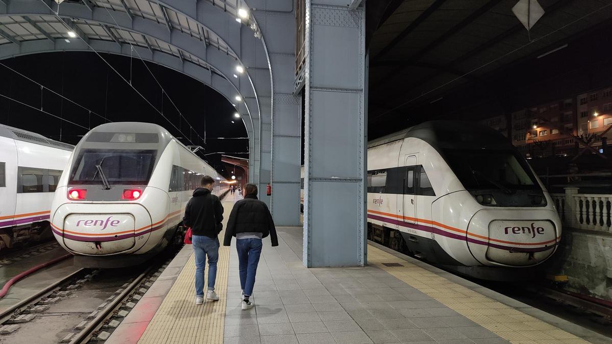 Dos viajeros ante un tren madrugador del Eje Atlántico en A Coruña