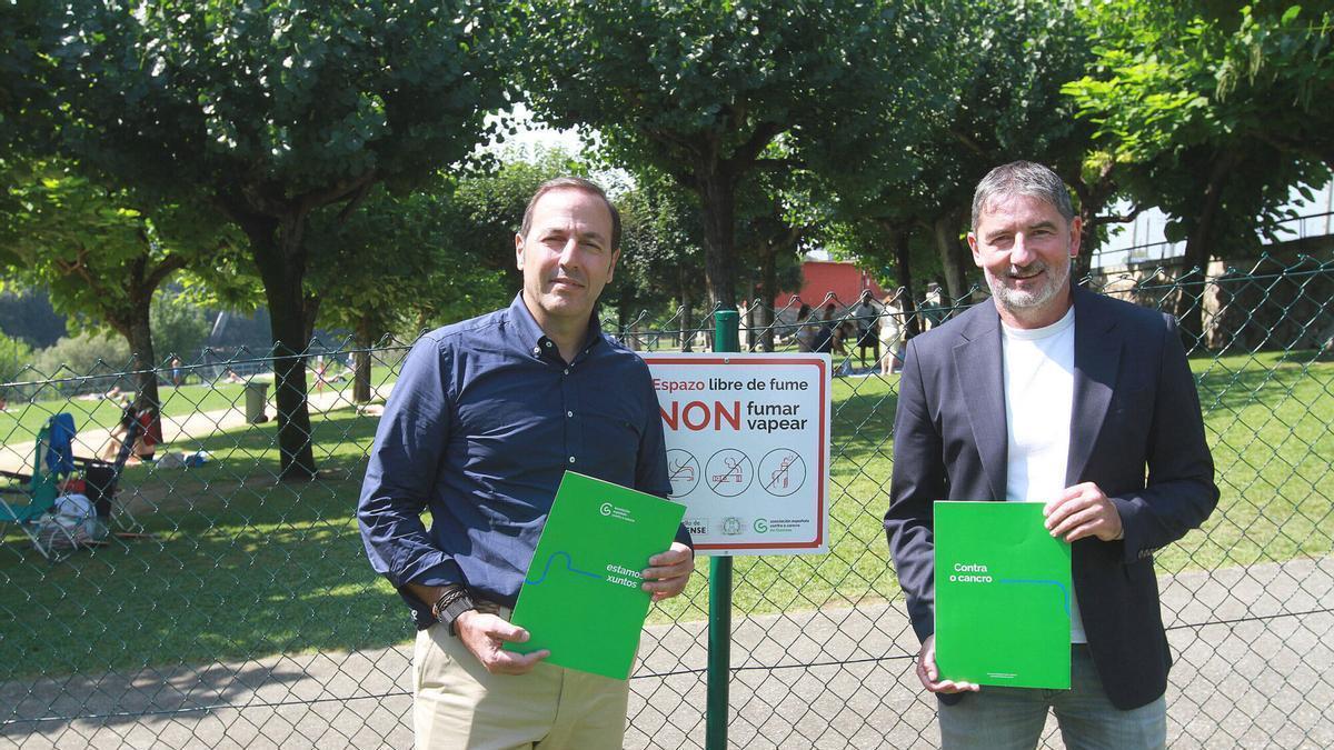 Germán Rodríguez y Aníbal Pereira colocando el cartel de "No fumar" en las piscinas de Oira
