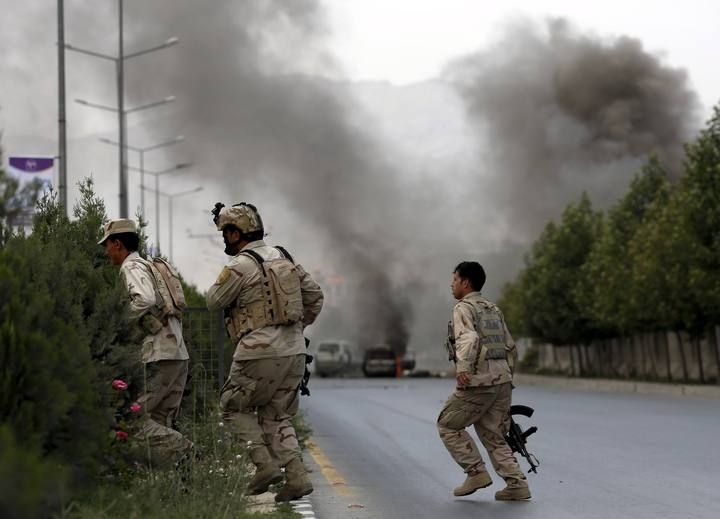 Members of Afghan security forces cross a road as smoke billows from the site of an attack near the Afghan parliament in Kabul, Afghanistan