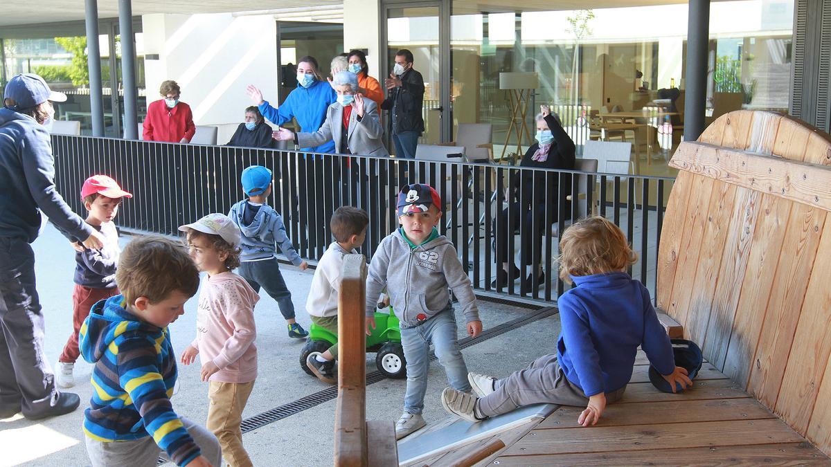 Un grupo de niños de la escuela infantil, jugando ayer ante la mirada de los mayores del centro de día. // IÑAKI OSORIO