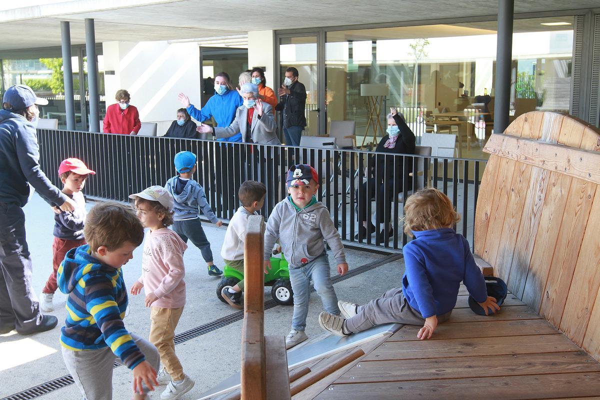 Un grupo de niños de la escuela infantil, jugando ayer ante la mirada de los mayores del centro de día. // IÑAKI OSORIO