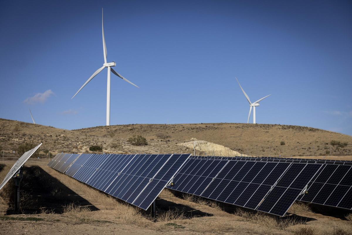 Imagen de archivo de un parque fotovoltaico, con aerogeneradores al fondo.