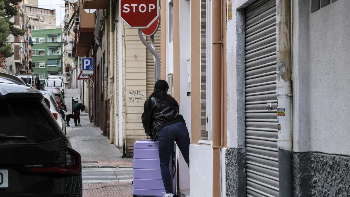 Una mujer sale con maletas de un portal en el barrio de Carolinas.