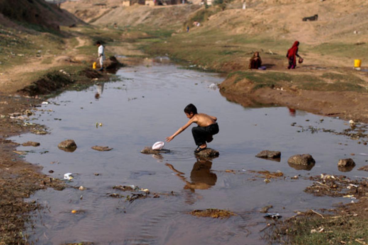 Un nen refugiat afganès intenta agafar el seu barret en un riu dels afores d’Islamabad (Pakistan).