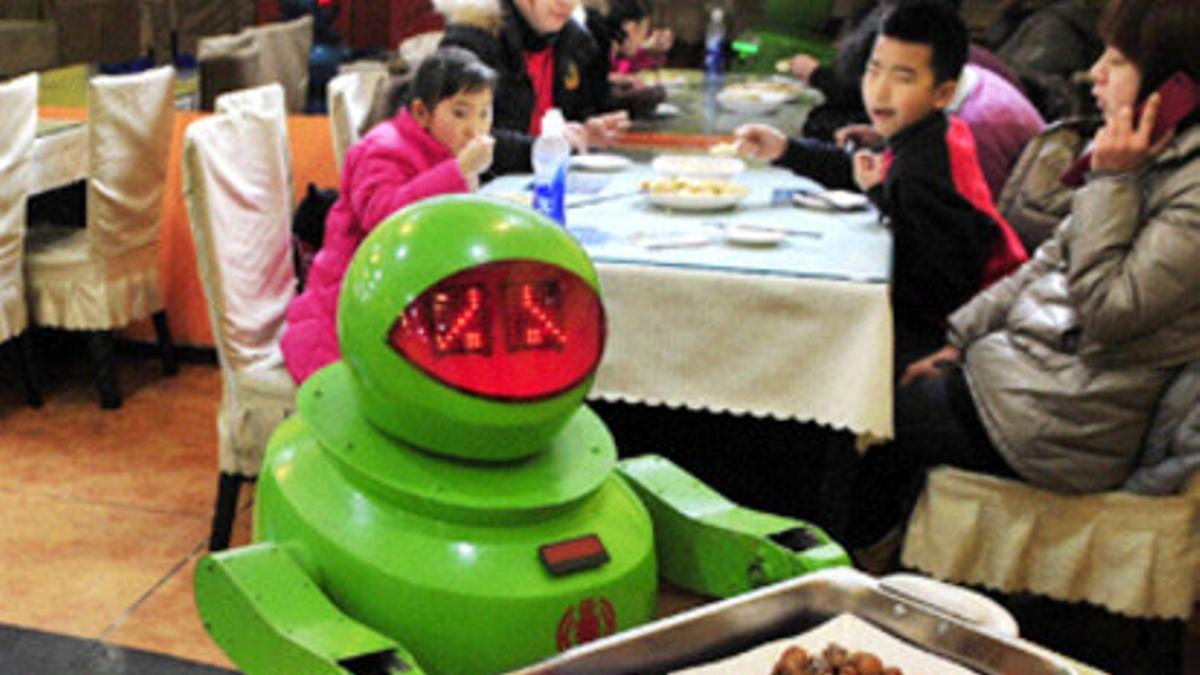 El androide sirve la comida ante la atenta mirada de unos niños.