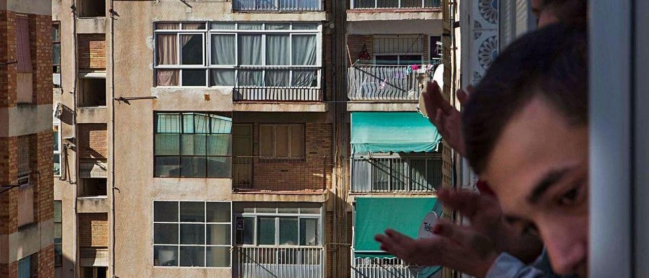 Un grupo de personas asomadas a una ventana de un bloque de viviendas en un barrio de Alicante.