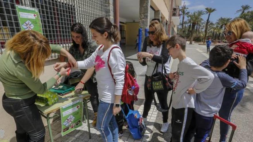 Madres y alumnos en la venta de pulseras para recaudar fondos ayer en el patio del colegio Reyes Católicos de Elche.