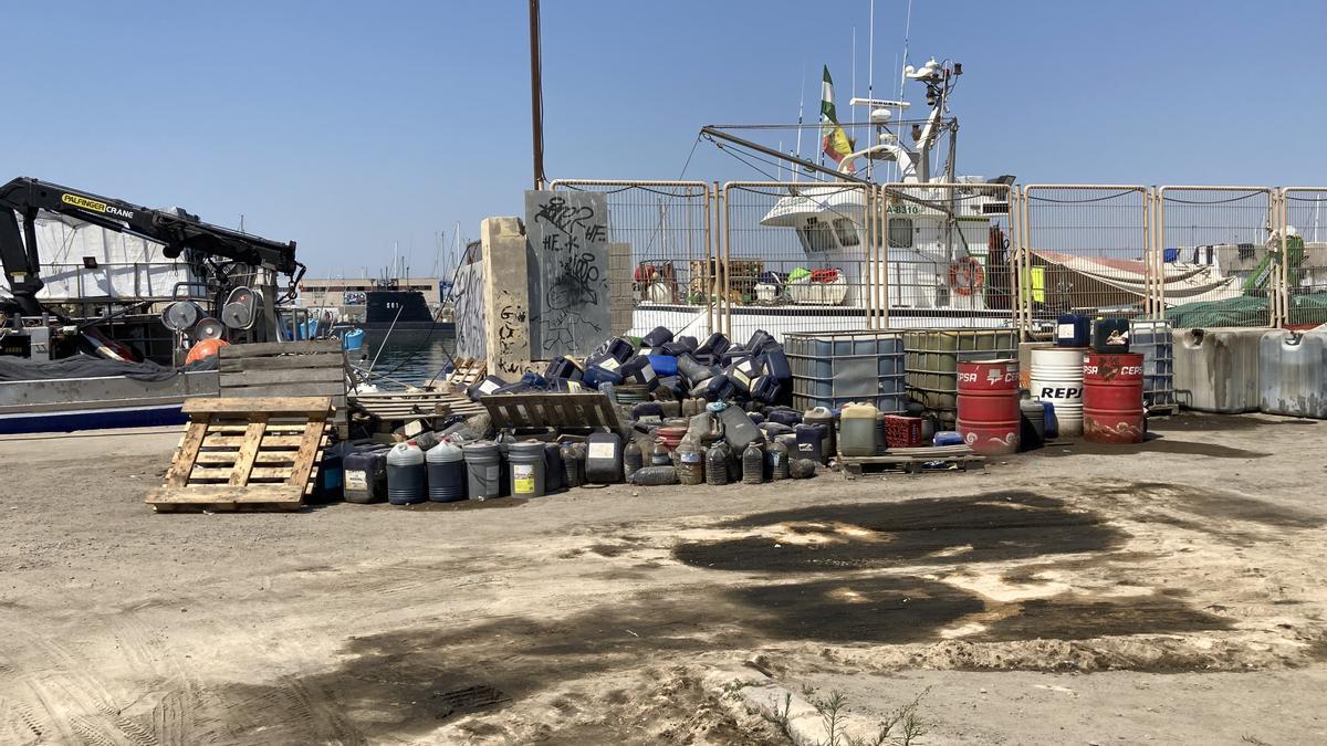 Palés, garrafas, barriles  se acumulan junto a las embarcaciones atracadas en el puerto pesquero y la lonja