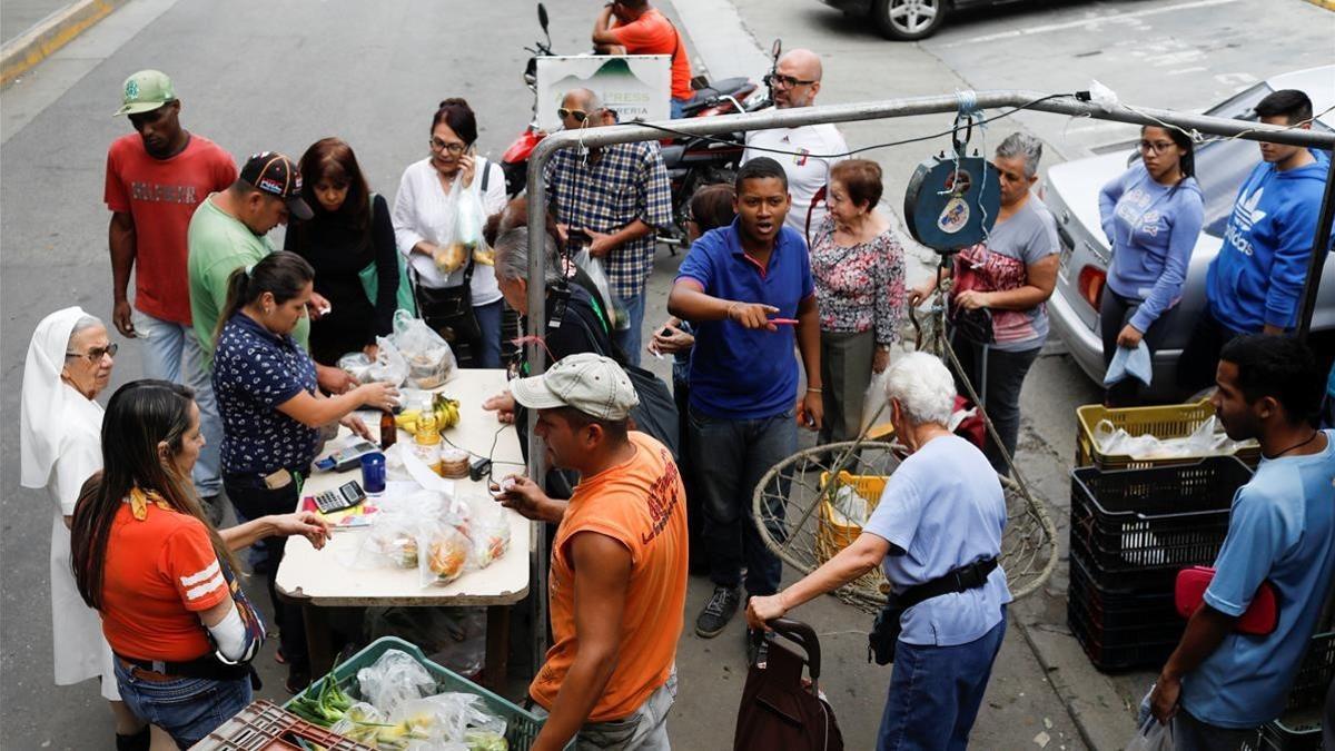 Venezolanos hacen cola para pagar la fruta y las verduras en un mercado callejero, en Caracas, el 13 de noviembre.