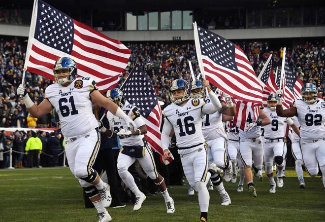 Los jugadores de los Guardiamarinas de la Marina de la Academia Naval de los Estados Unidos (USNA) llegan ondeando la bandera estadounidense antes del juego anual de fútbol del Ejército y la Marina en el Lincoln Financial Field en Filadelfia.