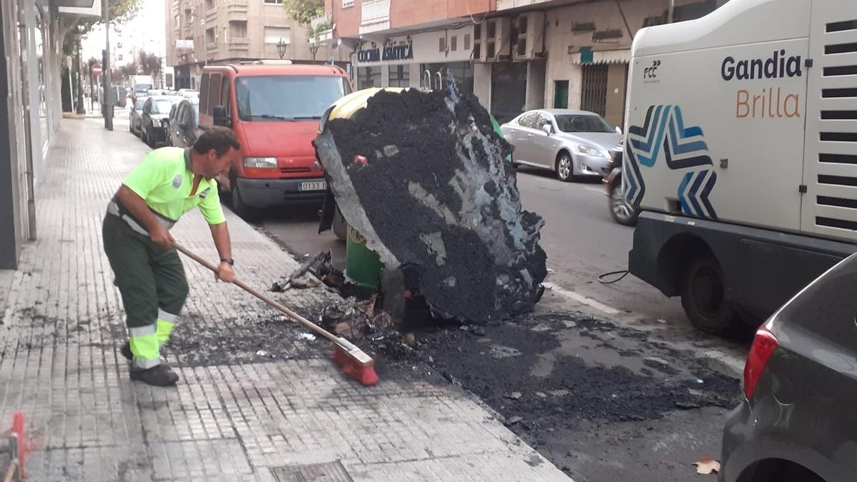 Un trabajador de la limpieza retira los restos de un contenedor quemado en València.