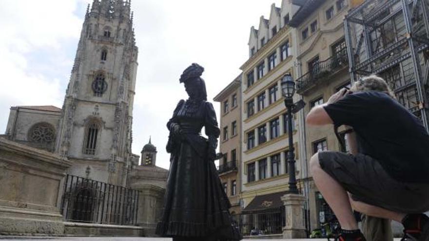 Un turista hace una fotografía de la Catedral ante la estatua de la Regenta.