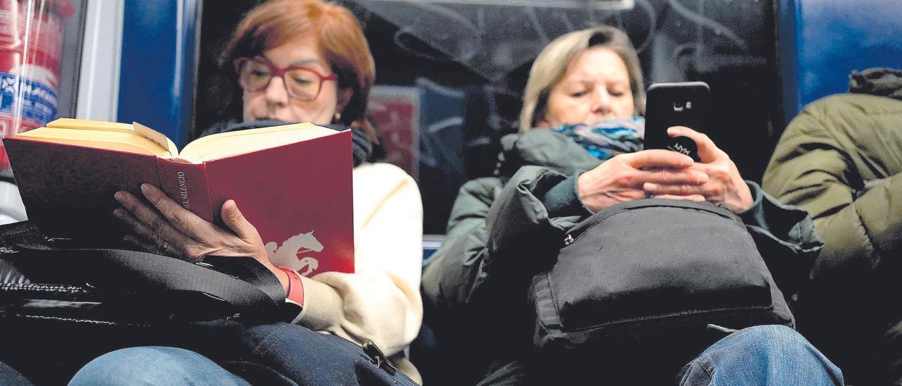 Una mujer ojea un libro y otra mira un teléfono móvil.