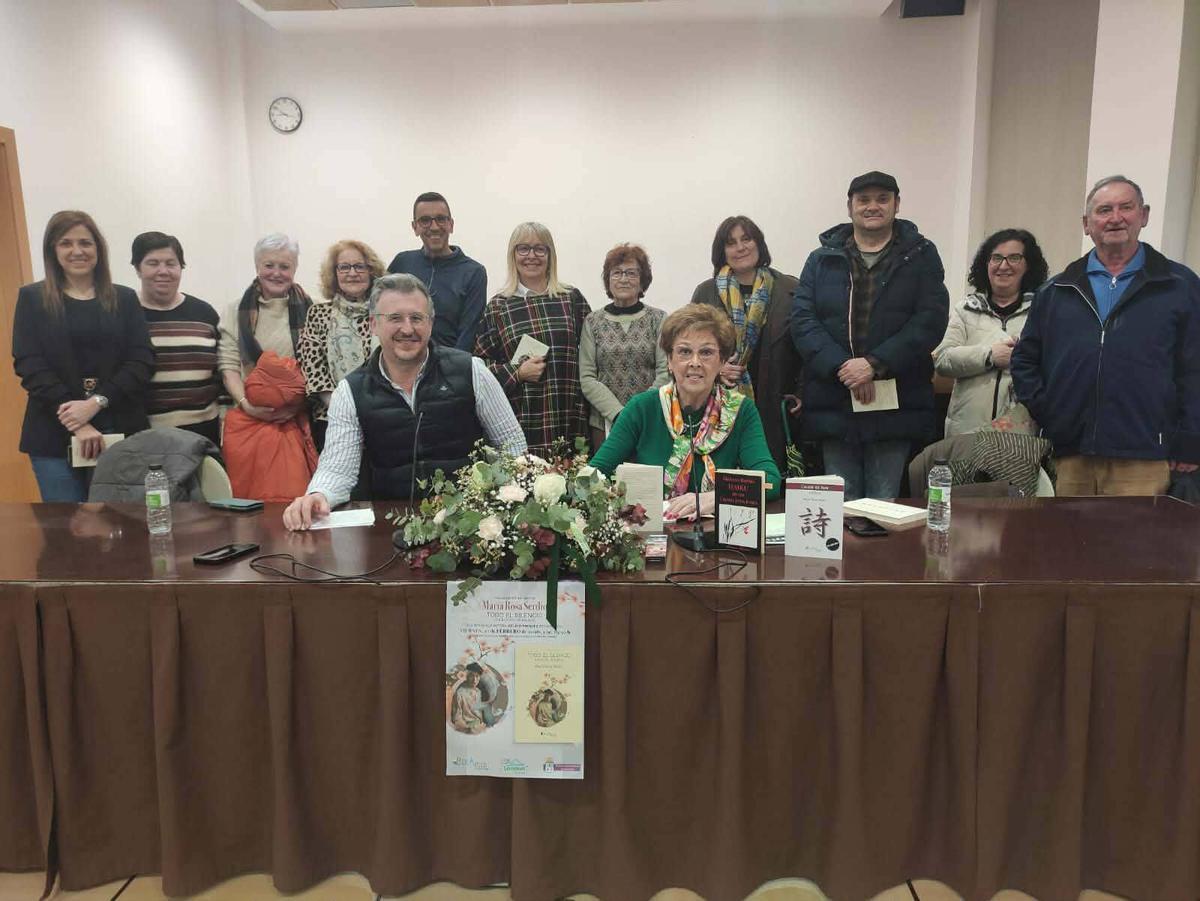 Pelayo Prendes y la autora, María Rosa Serdio, sentados, con varios asistentes a la presentación del libro.