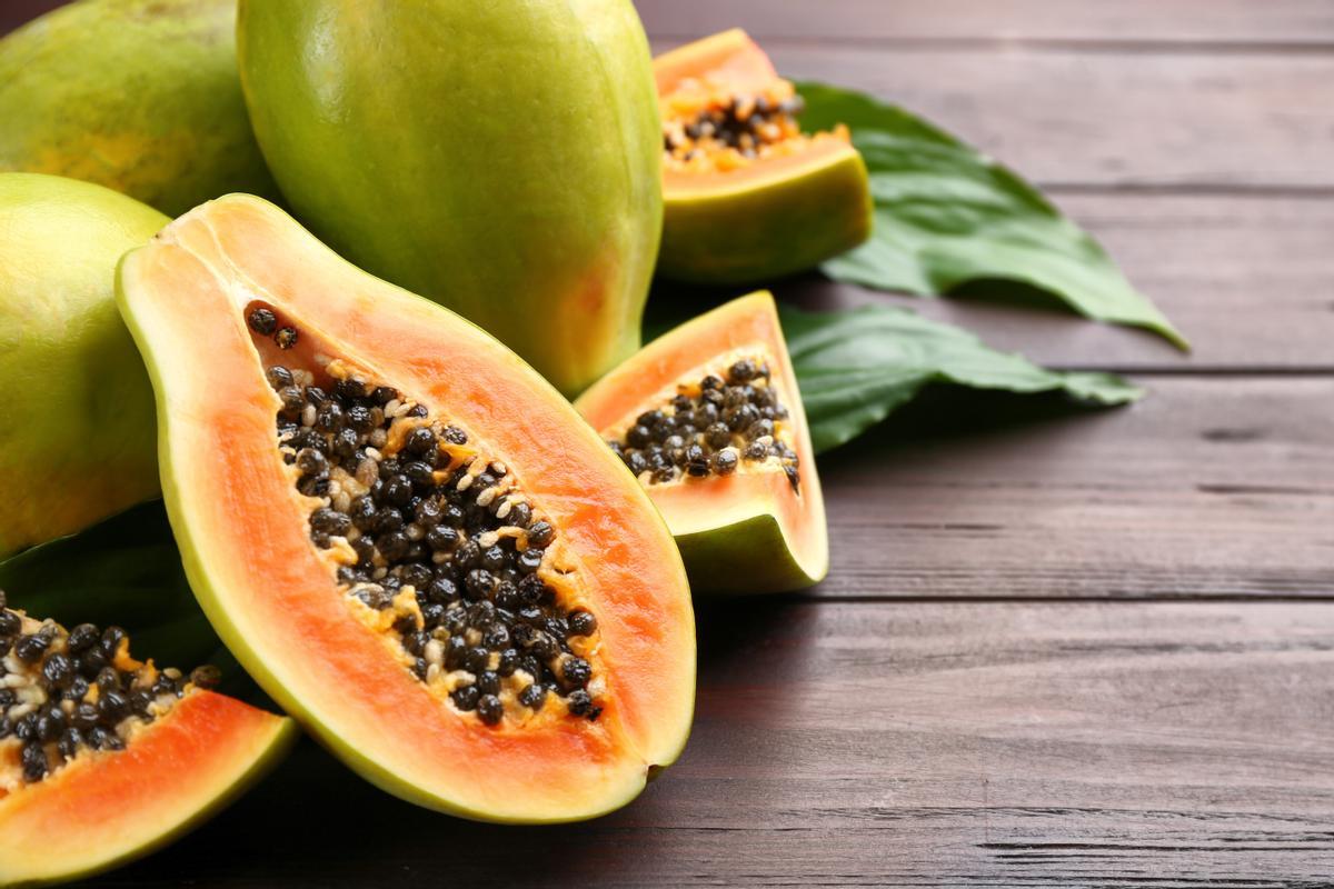 Fresh ripe papaya fruits with green leaves on wooden table. Space for text