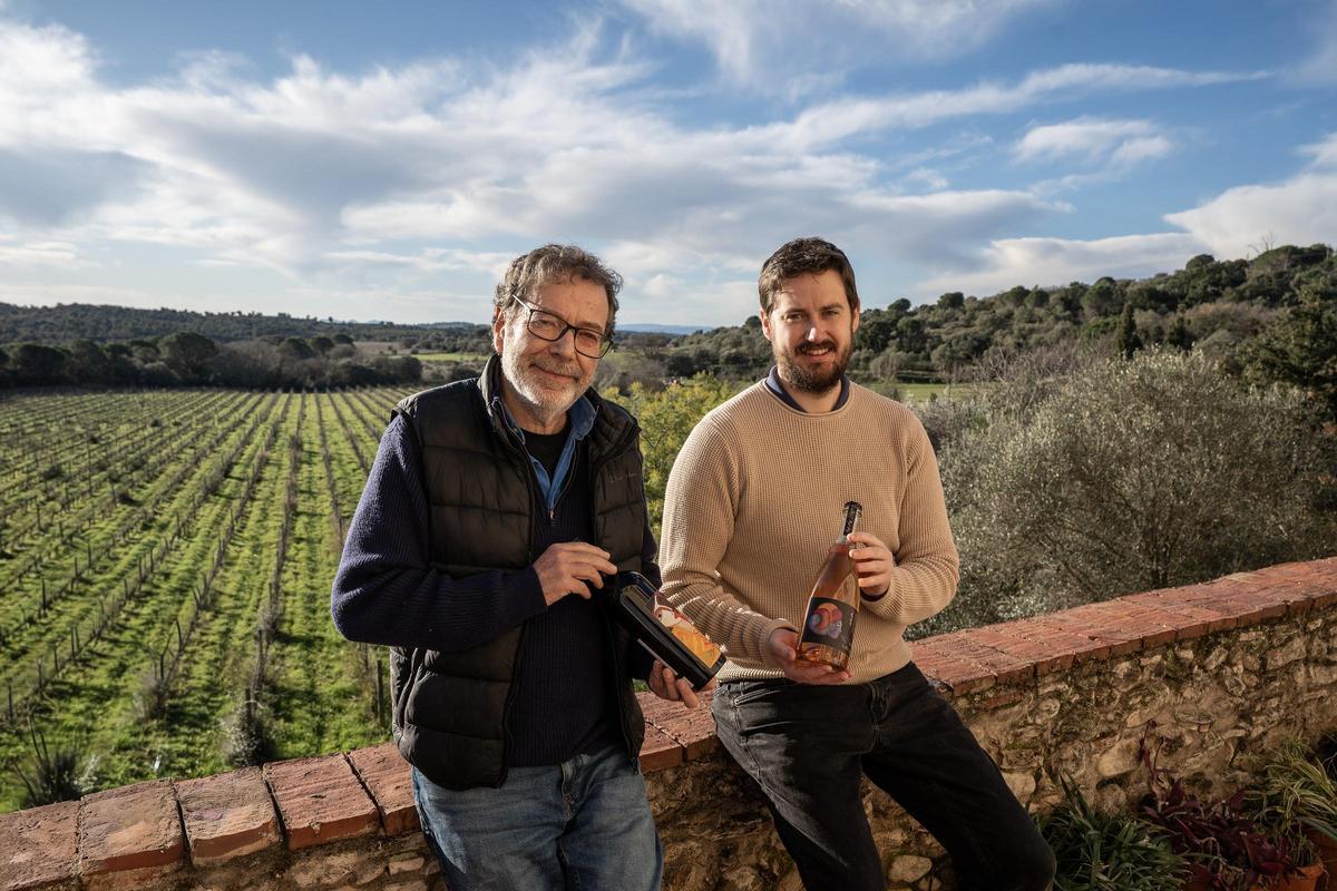 Joan i Gabriel Castelló, pare i fill, amb dos dels vins creats, el fruit de les vinyes que treballen i que veiem al fons.