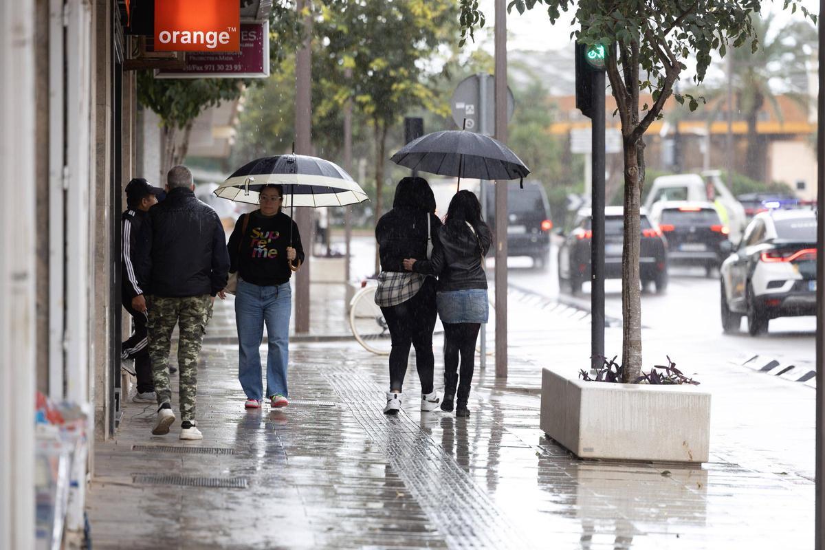 Pedestrians with umbrellas on a street in Ibiza this autumn.
