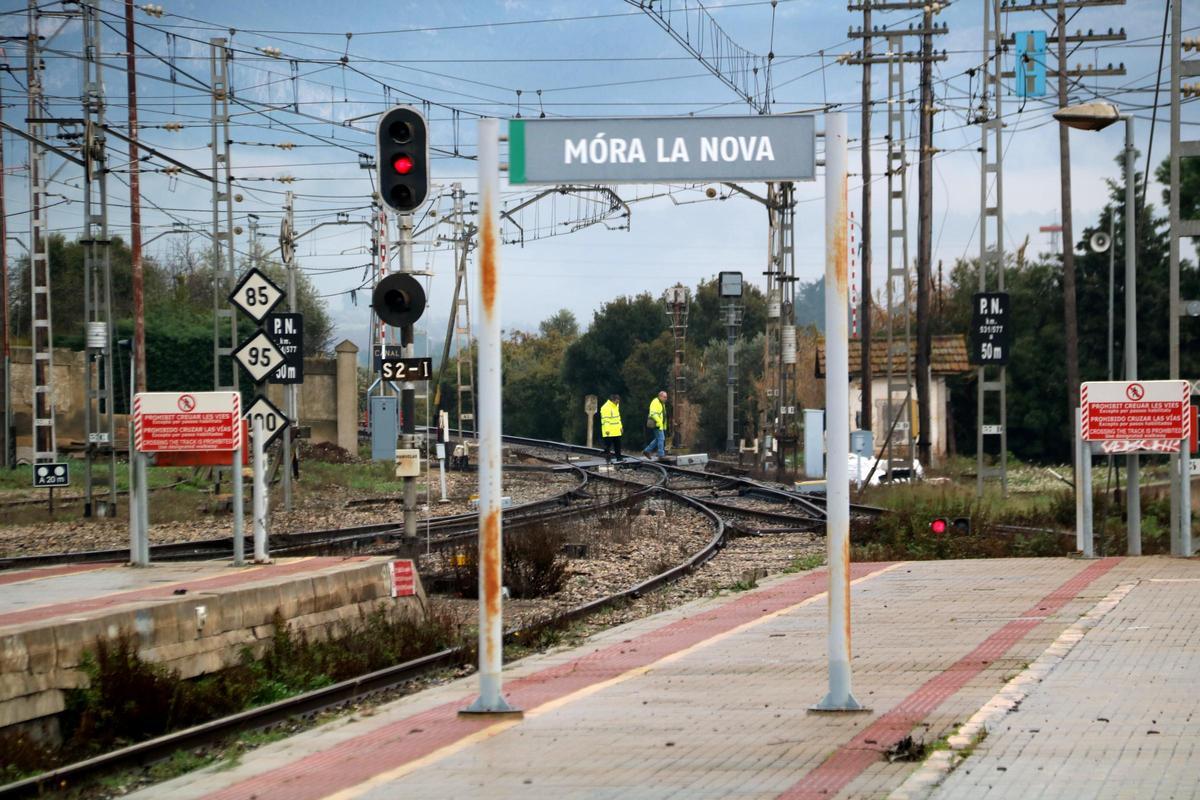 Cartells a l'estació de tren de l'R-15 a Móra la Nova, amb dos operaris al fons fent comprovacions a les vies