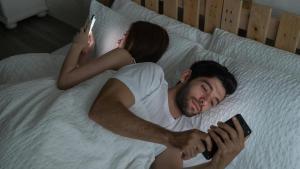 Una pareja usan sus teléfonos  en la cama