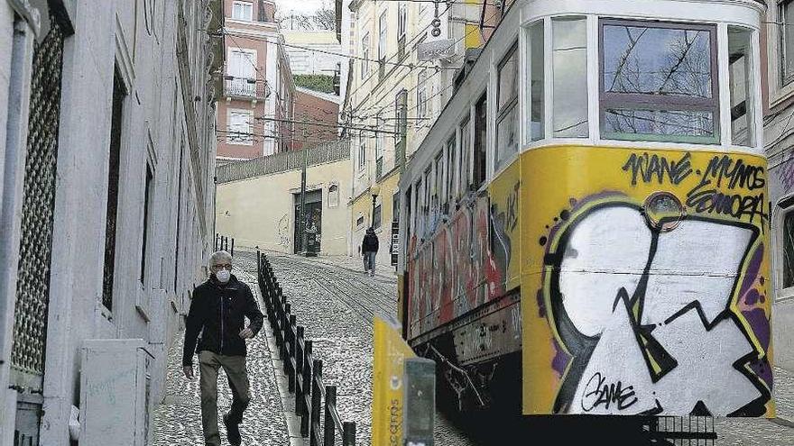 Un hombre con mascarilla camina por una calle de Lisboa, junto a un tranvía.